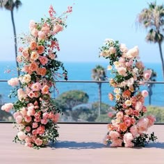 two tall vases filled with flowers sitting on top of a wooden floor next to the ocean