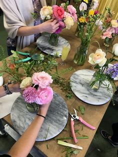 the woman is arranging flowers in vases on the table with scissors and other crafting supplies