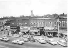 an old black and white photo of cars parked in front of stores on a city street