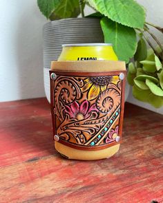 a can cooler sitting on top of a wooden table next to a potted plant