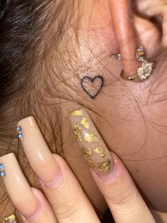 a close up of a person's ear with gold nail polish and piercings