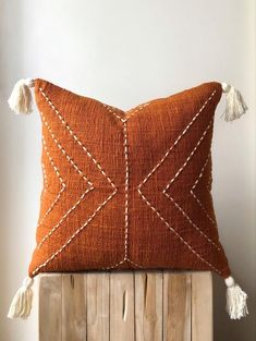 an orange pillow with white stitches and tassels sits on top of a wooden crate