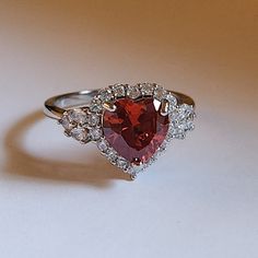 a red heart shaped diamond ring sitting on top of a table