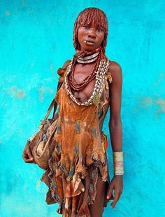 a woman in an ethnic dress stands against a blue wall