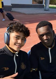 two young men sitting next to each other on a tennis court with headphones on