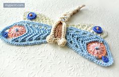 a crocheted butterfly ornament is shown on a white tablecloth with blue and pink flowers