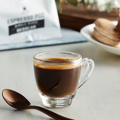 a cup of coffee sitting on top of a table next to a spoon and bag