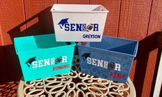 three different colored boxes sitting on top of a metal table next to a wooden fence