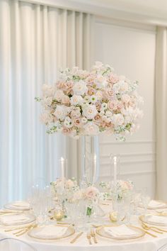 a tall vase filled with white and pink flowers on top of a table covered in plates