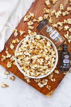 a wooden cutting board topped with a bowl of popcorn next to a bottle of maple syrup