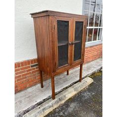 a wooden cabinet sitting on the side of a road next to a brick wall and window