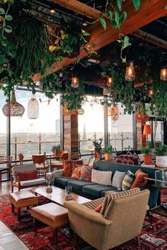 a living room filled with lots of furniture and plants hanging from the ceiling above it