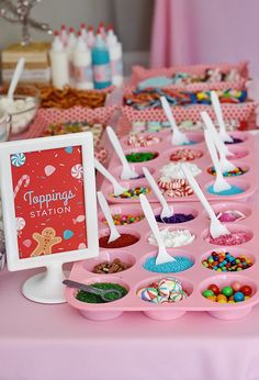 a pink table topped with lots of cupcakes and desserts next to a sign