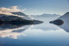 the mountains are reflected in the still water on this calm day with blue sky and clouds