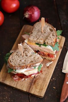 two halves of a sandwich sitting on top of a wooden cutting board next to tomatoes