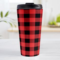 a red and black plaid pattern travel mug on a white table with a potted plant in the background