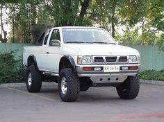 a white pick up truck parked in a parking lot next to a green fence and trees