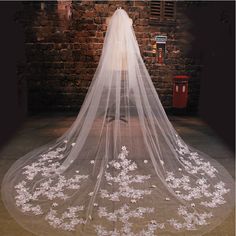 the back of a bride's veil with flowers on it is shown in front of a brick wall