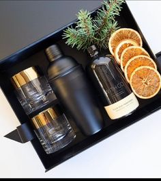 an assortment of bottles and oranges in a black tray with pine branches on top