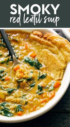 a white bowl filled with red lentula soup and topped with spinach, bread