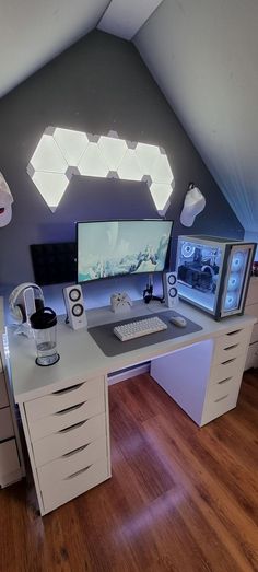 a computer desk with two monitors on top of it in an attic office space that has wooden floors and white walls