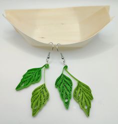 two green leaf shaped earrings on a white surface