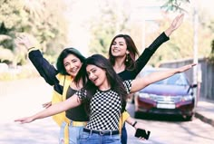 three young women standing on the side of a road with their arms in the air