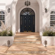 an entrance to a large white house with black door and two potted plants on the steps