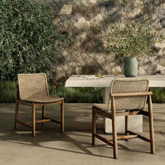 two chairs and a table in front of a stone wall with greenery on it