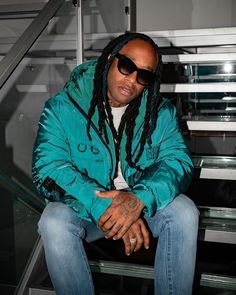 a man with dreadlocks sitting on top of a set of stairs wearing sunglasses