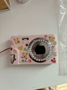 a pink camera sitting on top of a white table next to a plastic bag with teddy bears