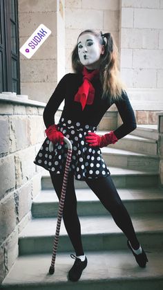 a woman dressed up as a clown with a cane and polka dot dress, standing on some steps