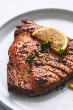 a piece of steak on a white plate with lemon wedges and parsley garnish