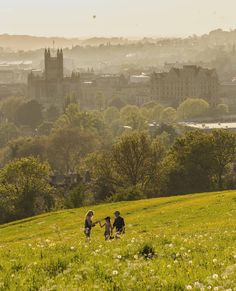 two people are walking in the grass with buildings in the background