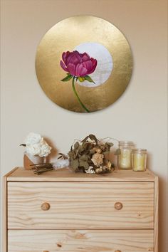 a dresser with flowers and candles on it in front of a gold circle wall art