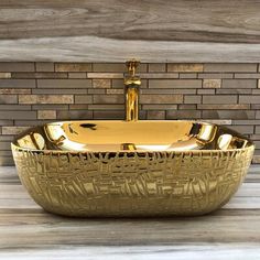 a gold sink sitting on top of a wooden floor next to a brick wall with a faucet