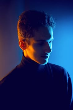 a man in a black turtle neck shirt looking at his cell phone while standing against a blue background