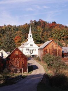 an old church sits on the side of a country road in front of autumn foliage