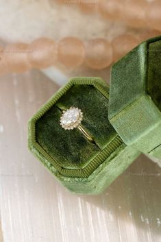 an open green velvet ring box with a white diamond in it's center on a table