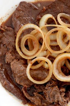 some onion rings are on top of beef in a brown sauce with gravy