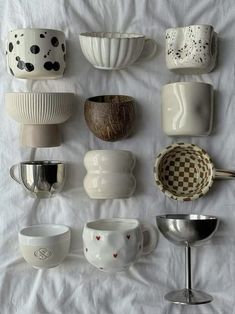 there are many different cups and bowls on the white tablecloth, one is empty