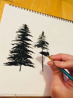 a person is holding a pencil in their hand and drawing trees on paper with black ink