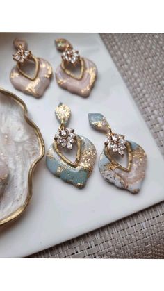 four pairs of earrings sitting on top of a white plate next to a seashell