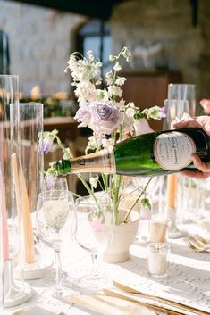 a person pours champagne into a glass at a table with flowers and glasses on it