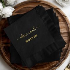 three black napkins with gold lettering on them sitting on a wooden plate next to flowers