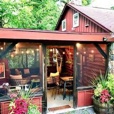 a red shed with patio furniture and lights on the front door is surrounded by greenery