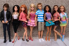 a group of dolls standing next to each other in front of a wall with clothes on