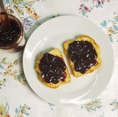 two pieces of bread with jam on them sitting on a plate next to a jar of jelly