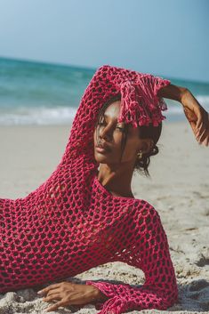 a woman laying on the beach in a pink crocheted shawl and head scarf