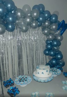 blue and silver balloons are hanging over a table with cake, cupcakes, and other decorations